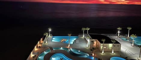A resort with multiple swimming pools, palm trees, and a sunset view.