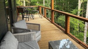 Eine überdachte Terrasse mit Korbmöbeln und einem Tisch, umgeben von einem Holgitter und mit Blick auf einen Wald.