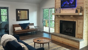 Ein modernes Wohnzimmer mit Kamin, Deckenventilator, Wand-Fernseher und großem Fenster.