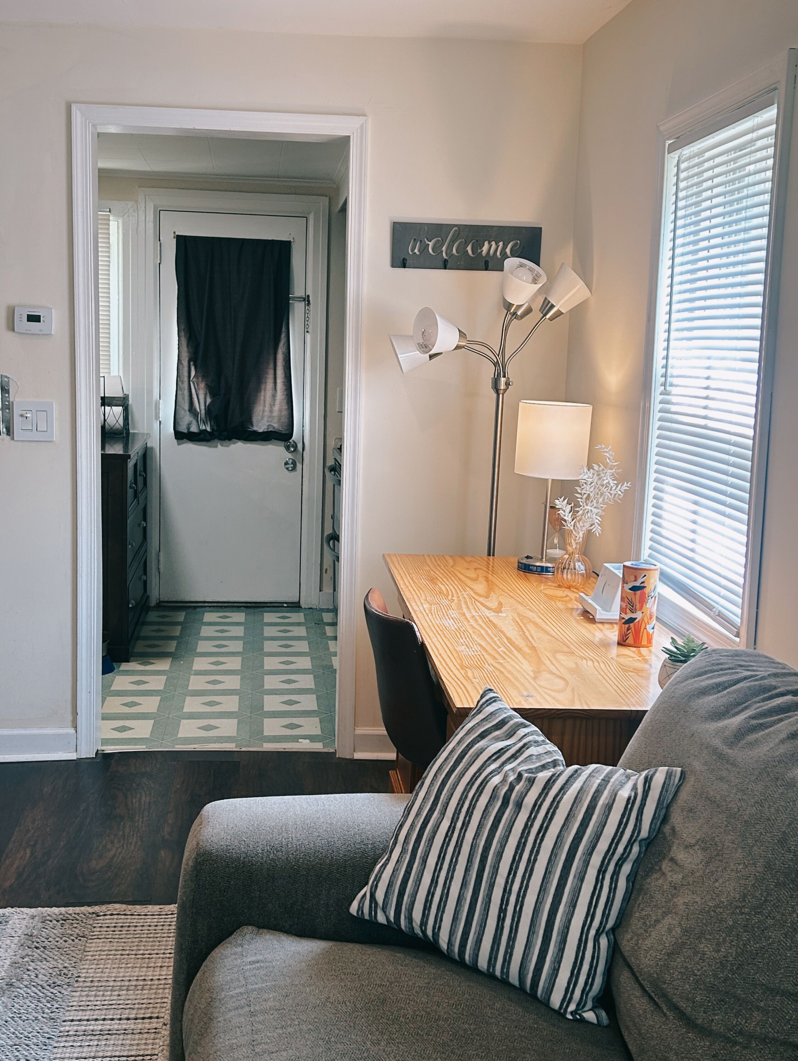 Un salon chaleureux avec une table à manger en bois, un canapé orné de coussins à rayures, une lampe et un panneau « Bienvenue » accroché au mur.