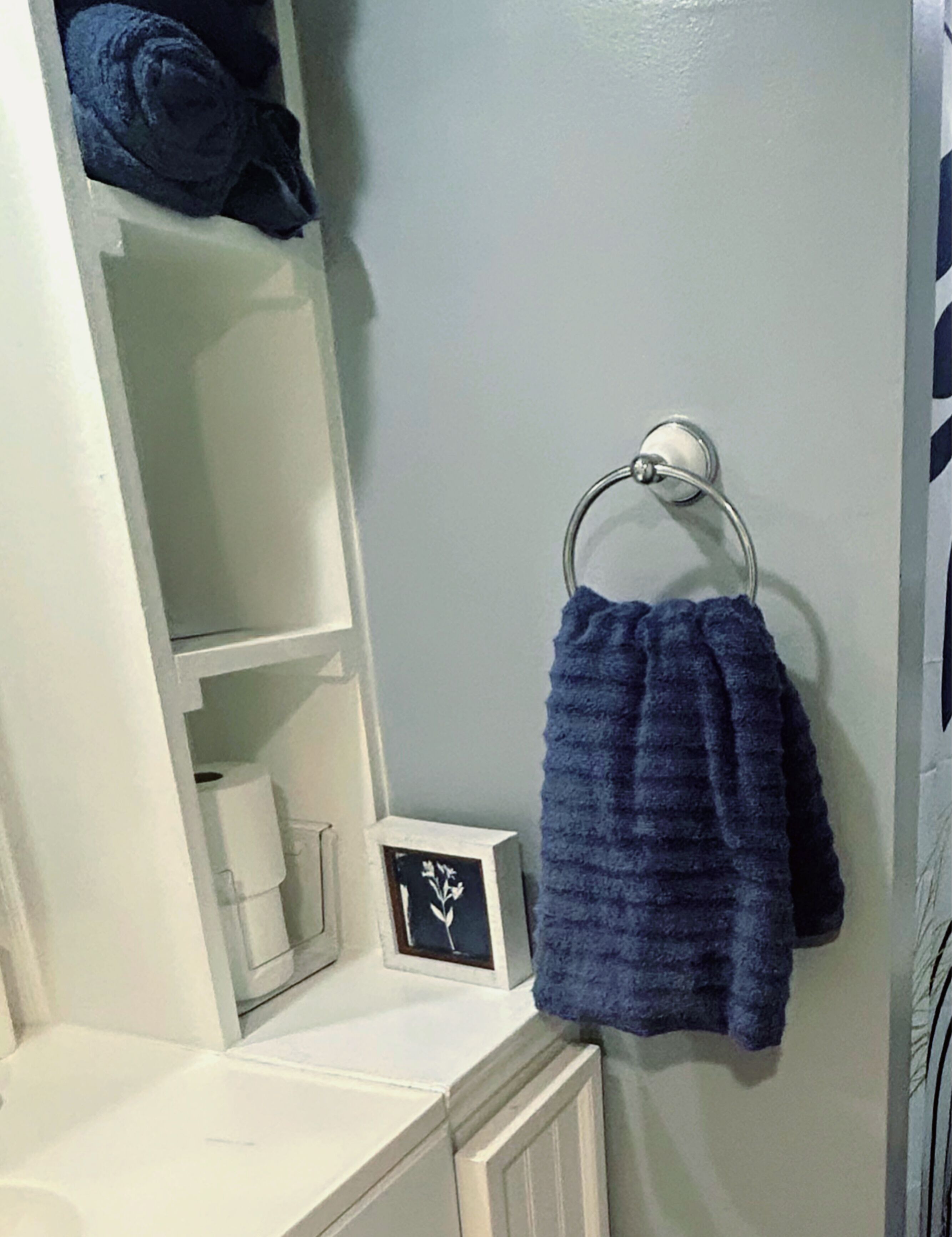 Uma casa de banho com toucador branco, um porta-toalhas com toalha azul e um quadro emoldurado no balcão.