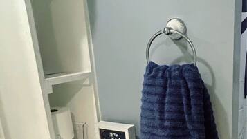 Uma casa de banho com toucador branco, um porta-toalhas com toalha azul e um quadro emoldurado no balcão.