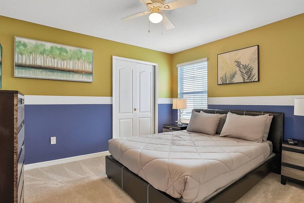 A bedroom with a bed, a nightstand, a lamp, and two wall-mounted paintings.