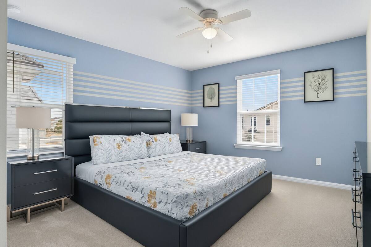 A bedroom with a bed, bedside tables, a ceiling fan, and windows with blinds.