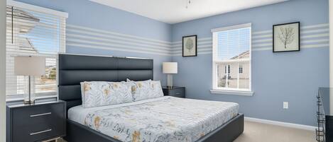 Un dormitorio con cama, mesitas de noche, ventilador de techo y ventanas con persianas.