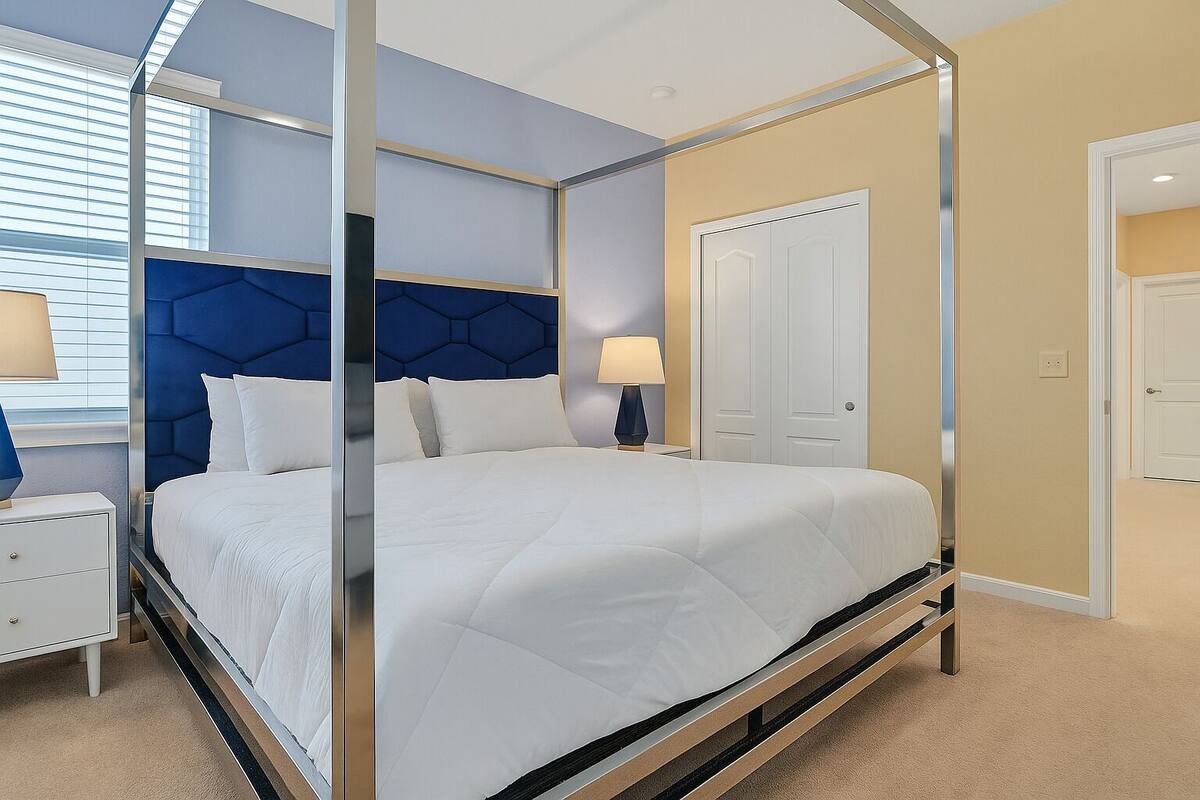 A modern bedroom with a four-poster bed, a nightstand, a lamp, and a wardrobe.