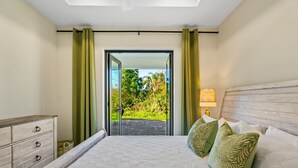A bedroom with a bed, a nightstand, a lamp, and a view of a garden through a glass door. - New 3BR , Near Myakka River, Boca Grande + Beach (Port Charlotte)