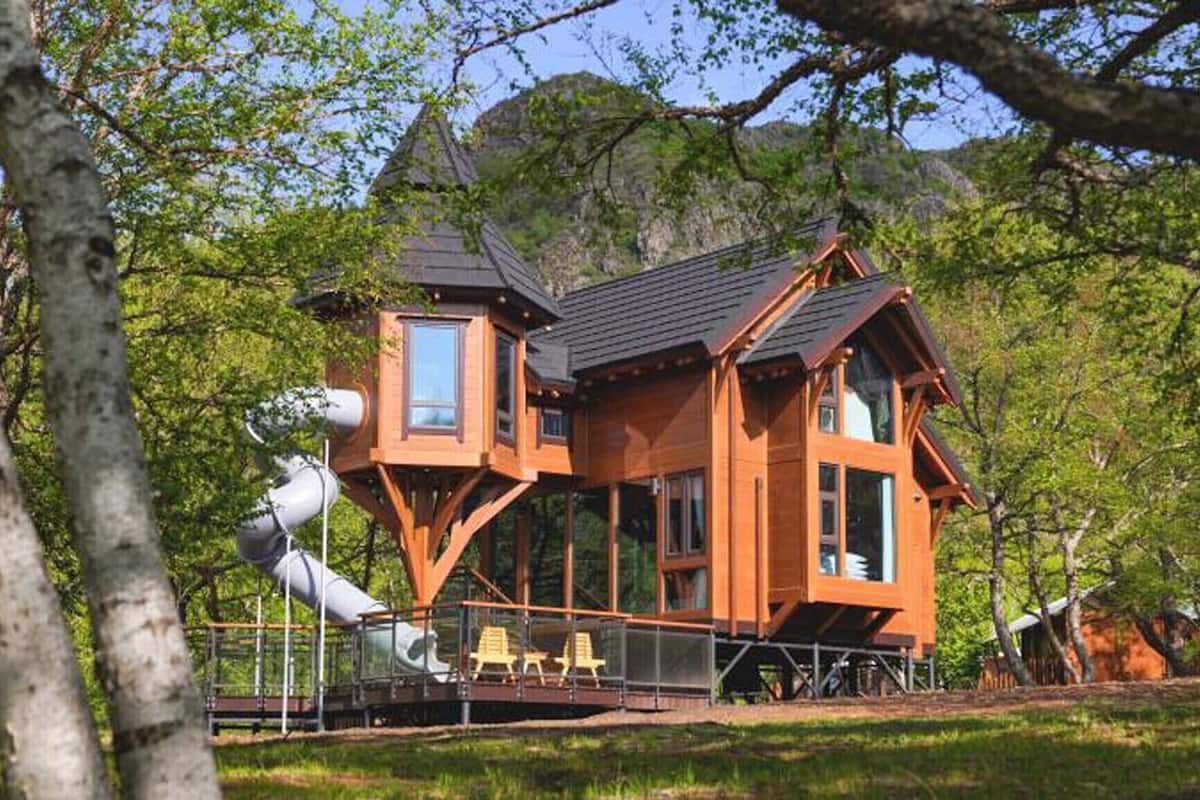 A wooden cabin with a balcony, a slide, and a large window.