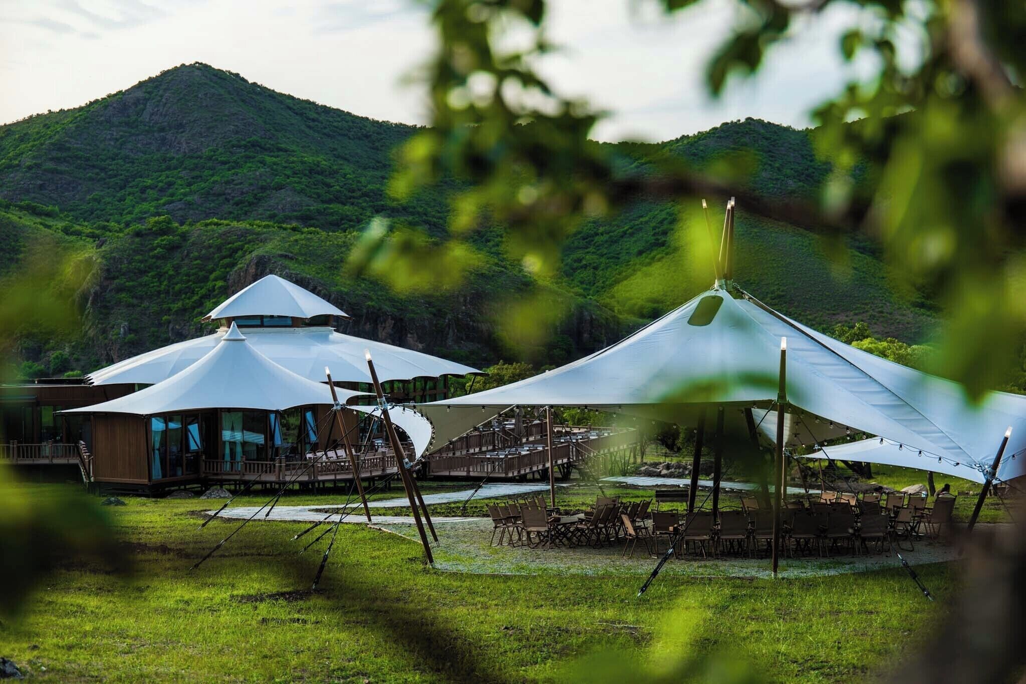 A yurt-style structure with a conical roof, surrounded by a grassy area with outdoor seating.