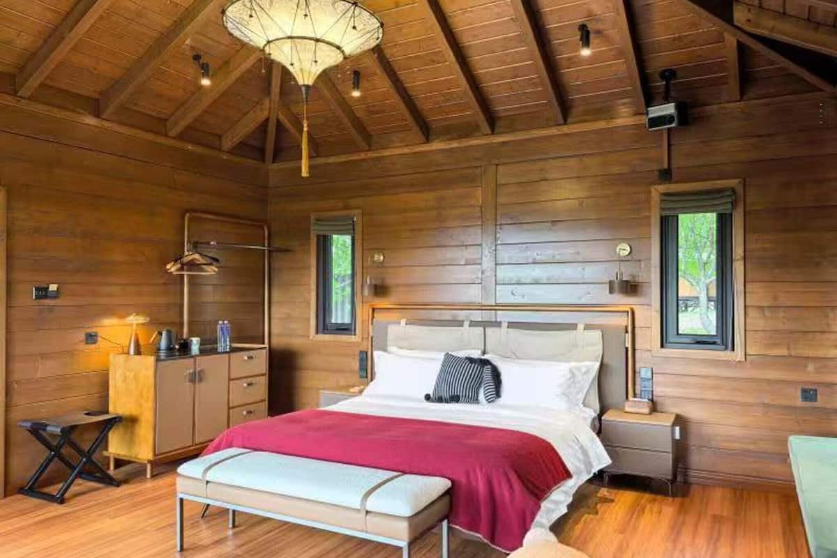 A wooden cabin bedroom with a bed, bedside tables, a bench, and a hanging light fixture.