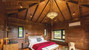 Un dormitorio de cabaña de madera con cama, mesitas de noche, un candelabro y una ventana.