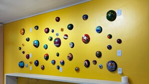 A room with a yellow wall displaying various helmets, a white counter, and black stools. - HOSTEL MANGUEIROSA (Belem)