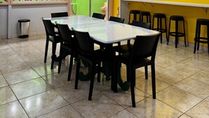 A conference room with a large table and chairs, a yellow wall with decorative plates, and a view through a window with a green fence. - HOSTEL MANGUEIROSA (Belem)