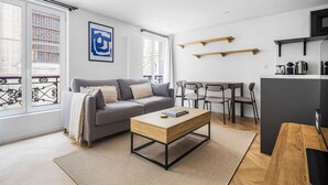 A modern living room with a grey sofa, a wooden coffee table, and a dining area with chairs. - Blueground | Le Marais, view, nr Place des Vosges (Paris)