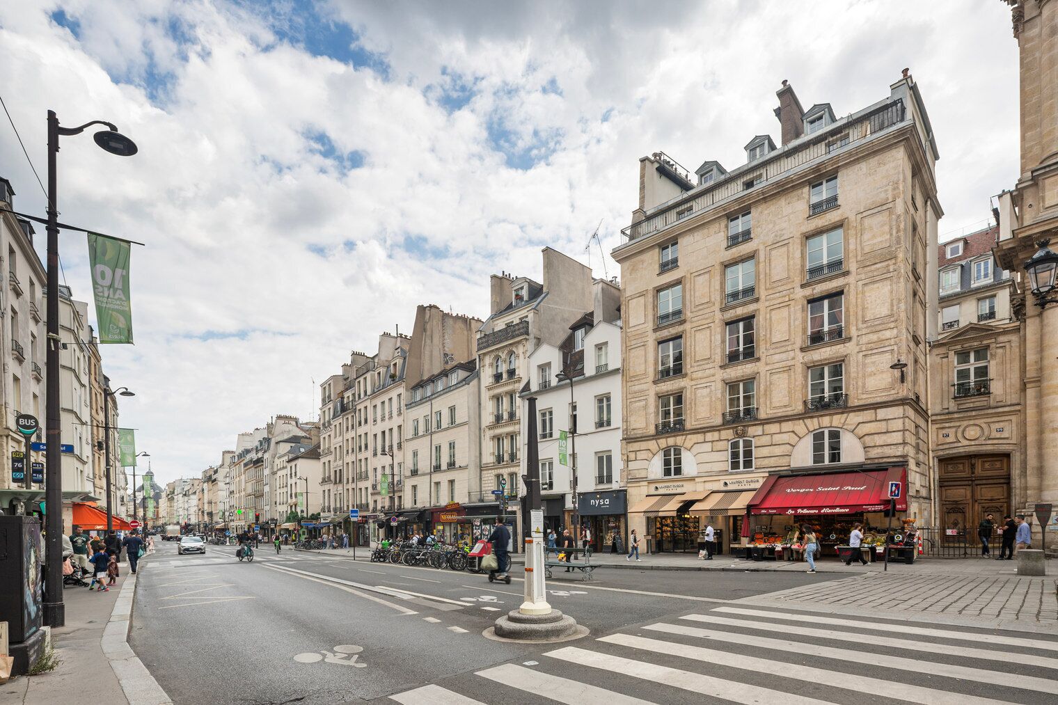 A bustling urban street with historic buildings, a crosswalk, and a variety of shops and cafes.