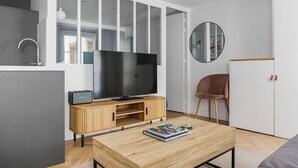 A modern living space with a flat-screen TV on a wooden TV stand, a small side table with a book, a round mirror, and a wardrobe. - Blueground | Le Marais, view, nr Place des Vosges (Paris)