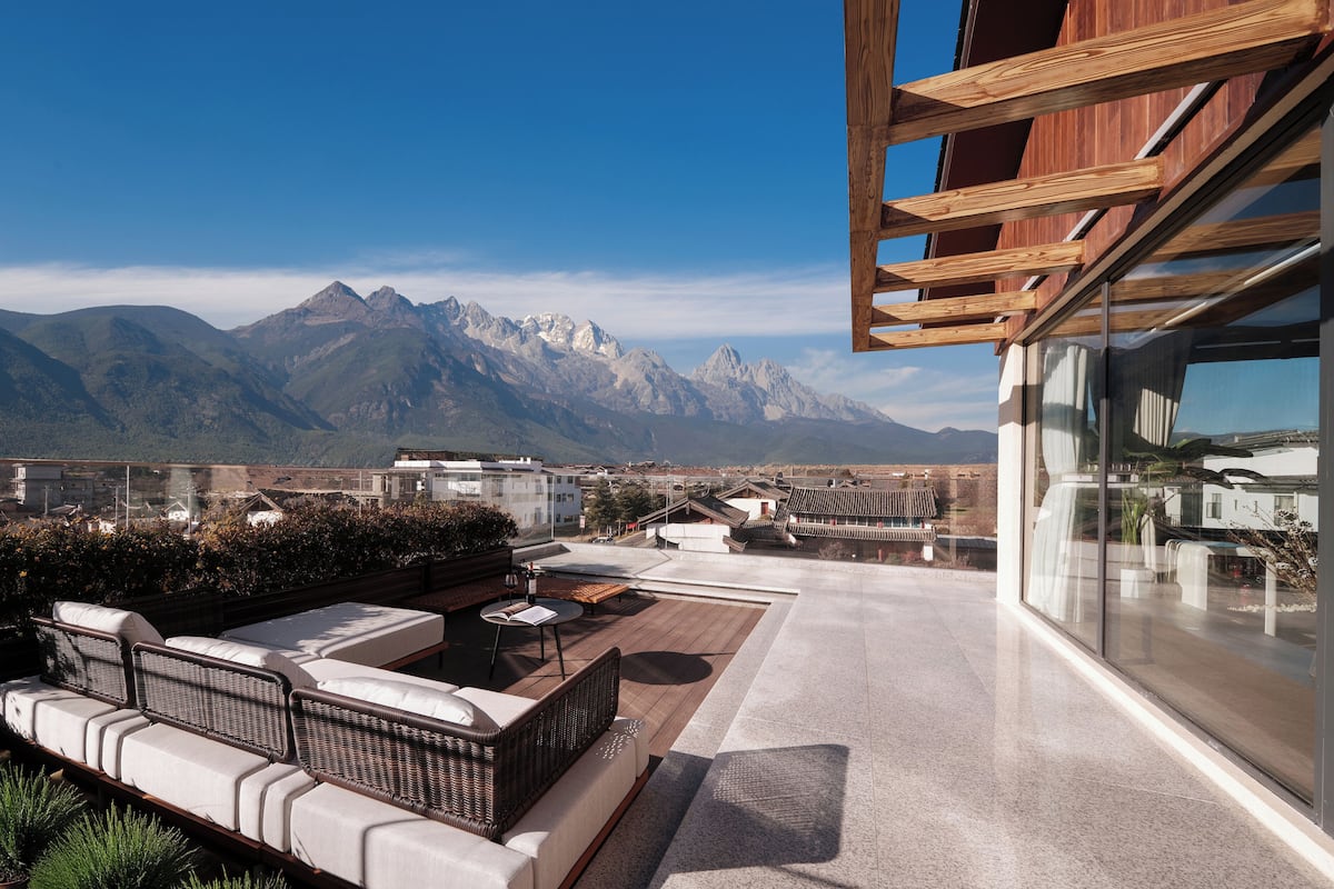 A rooftop terrace with outdoor seating, a view of mountains, and a modern building structure.