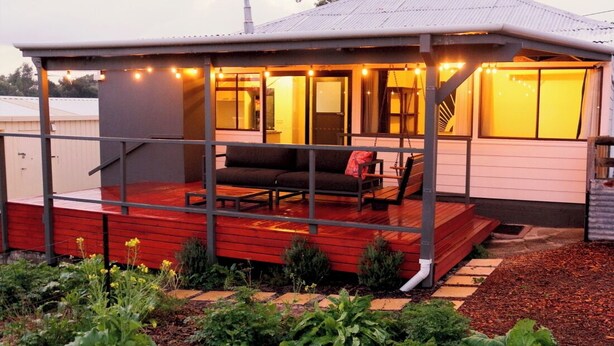A covered outdoor seating area with a red deck, a sofa, and a swing. - Jarrah Cottage, a renovated home with spacious block located in Waroona. (Waroona)