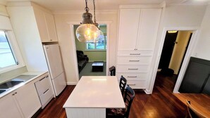 A compact kitchen with white cabinetry, a central island, and a hanging light fixture. - Jarrah Cottage, a renovated home with spacious block located in Waroona. (Waroona)