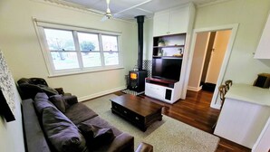 A living room with a sofa, coffee table, and a fireplace. There is a television and cabinets in the background. - Jarrah Cottage, a renovated home with spacious block located in Waroona. (Waroona)