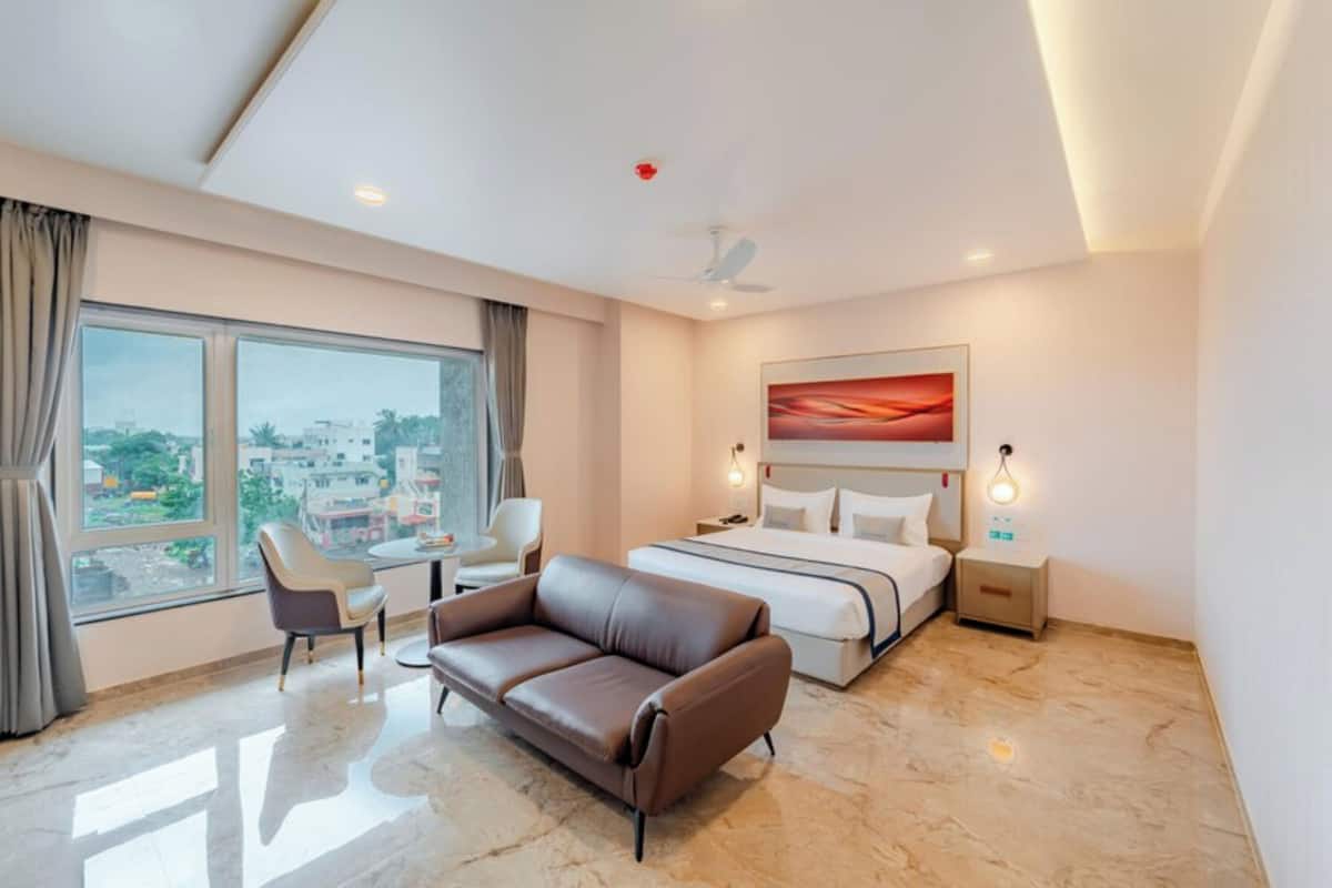 Une chambre d’hôtel équipée d’un lit, d’un canapé, d’un bureau et d’une grande fenêtre donnant sur la ville.