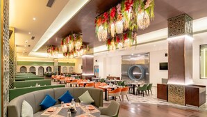 A restaurant with round tables, green booths, and hanging floral decorations. - Pravasa Hotel Vijayapura (Vijayapura)
