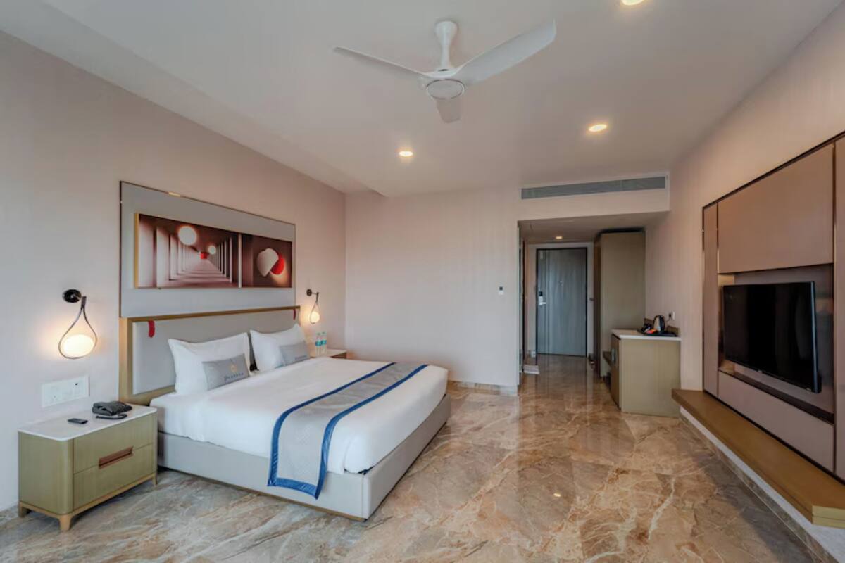 Une chambre d’hôtel moderne équipée d’un grand lit, d’un ventilateur de plafond, d’une télévision et d’une petite kitchenette.