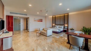 A modern hotel room with a bed, a sitting area, a desk, and a TV. - Pravasa Hotel Vijayapura (Vijayapura)