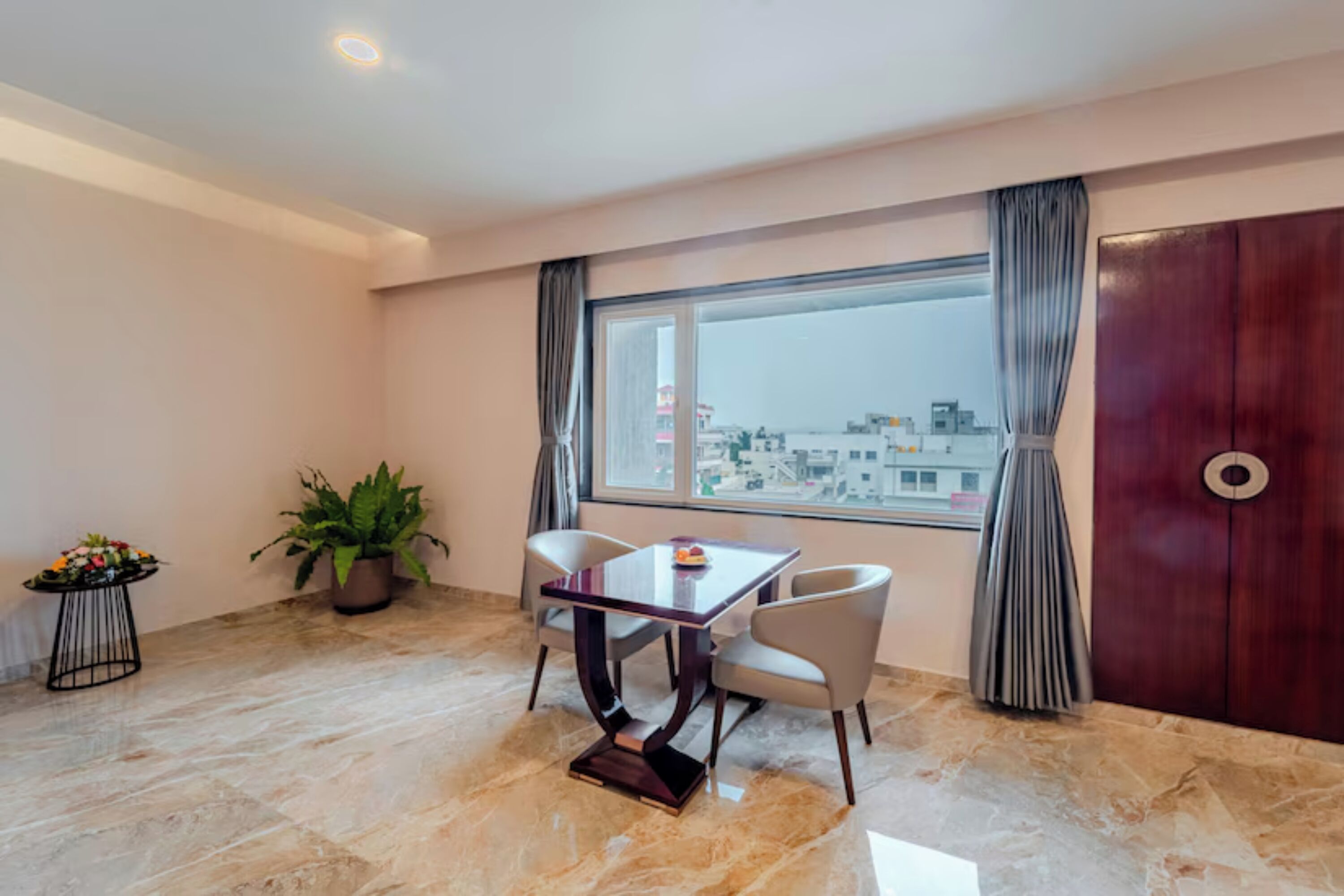 A room with a dining table, chairs, a potted plant, and a large window with curtains.