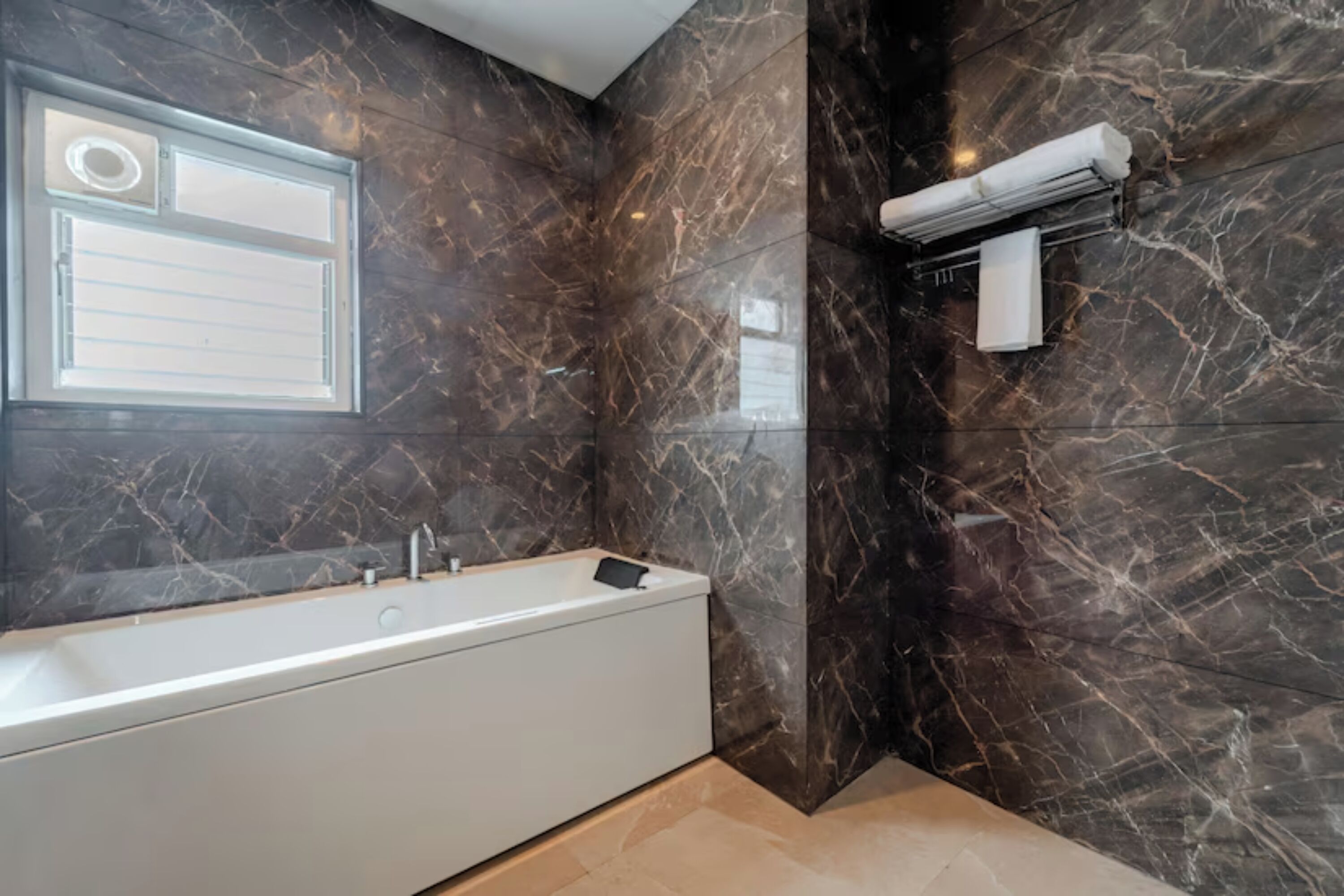 Une salle de bain moderne avec une baignoire blanche, des murs en marbre, un porte-serviettes et une fenêtre.