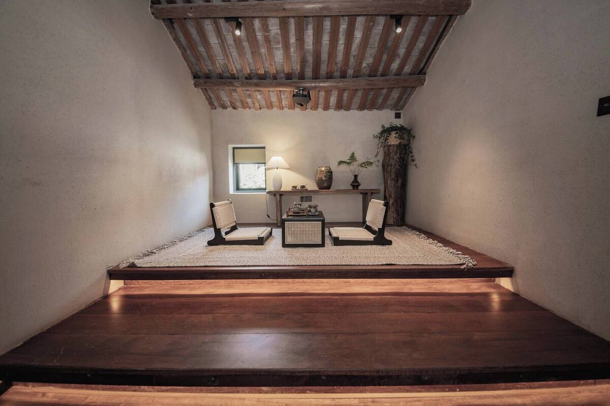 Un coin lecture confortable avec un banc en bois, deux fauteuils, une petite table et une lampe.