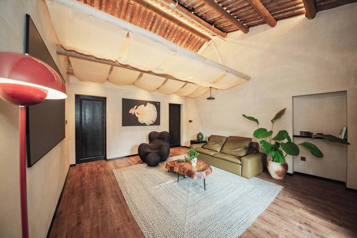 Un salon chaleureux avec un plafond en bois, un canapé vert, une table basse ronde et une grande plante en pot.