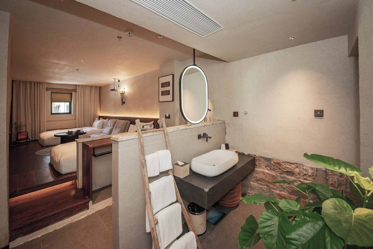 Une salle de bain d’hôtel moderne, dotée d’un grand miroir, d’un lavabo et d’un espace douche.