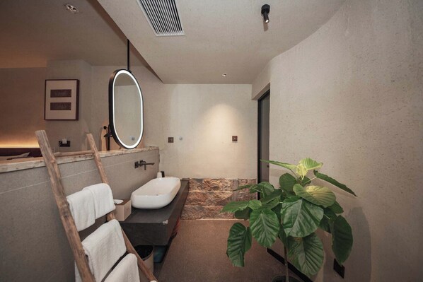 A modern bathroom with a large mirror, a sink, a towel rack, and a potted plant.