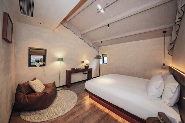 A bedroom with a large bed, a brown leather sofa, a small table with a lamp, and a window with a view.