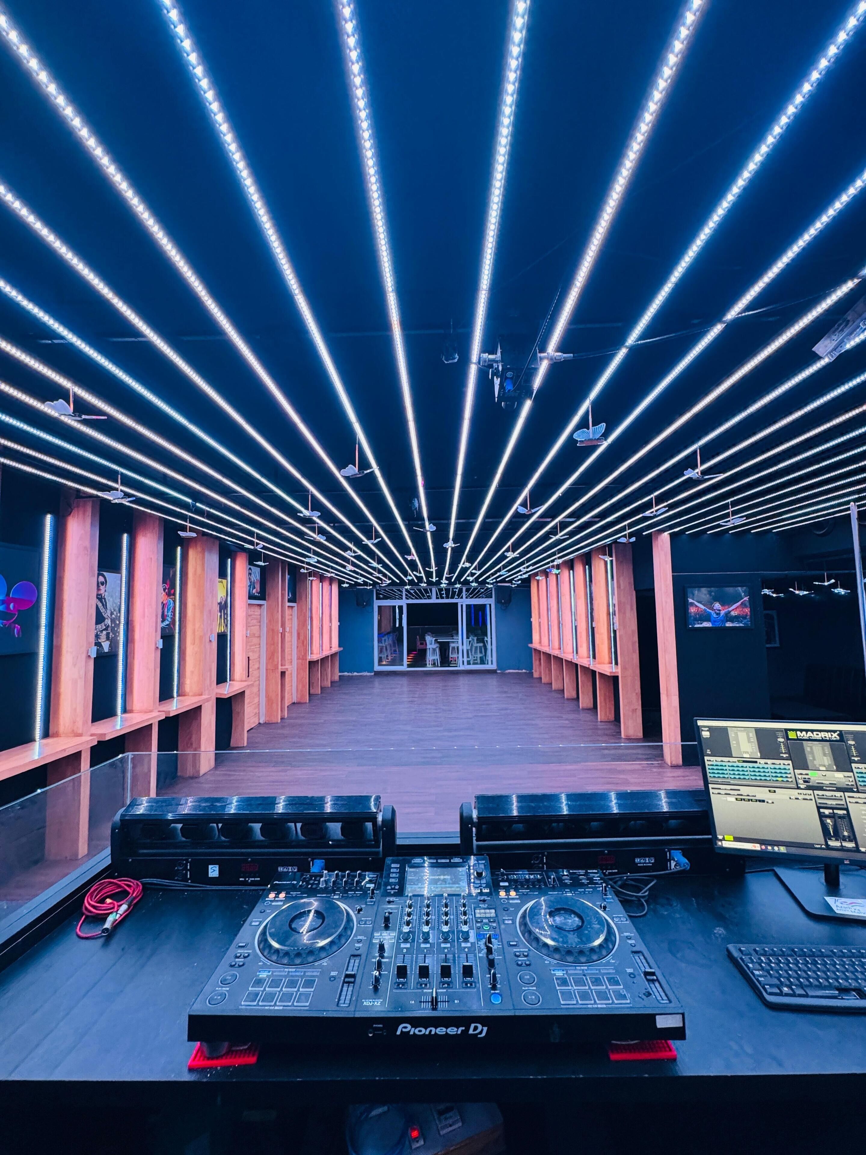 Una cabina de DJ con equipo Pioneer, iluminación LED y vista al salón.