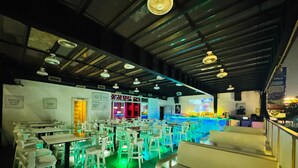 A restaurant with multiple tables and chairs, a bar area, and a stage for performances. - Cubix Hotel (Hubli)