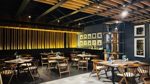 A restaurant with wooden tables and chairs, a patterned floor, and a dark wall with framed pictures. - Cubix Hotel (Hubli)
