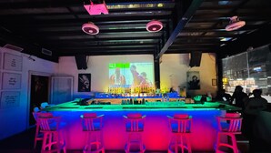 A bar area with a counter, stools, and a projection screen displaying a sports event. - Cubix Hotel (Hubli)