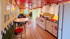 Une cuisine avec des meubles blancs, un plafond rouge et un coin repas comprenant une table et des chaises.
