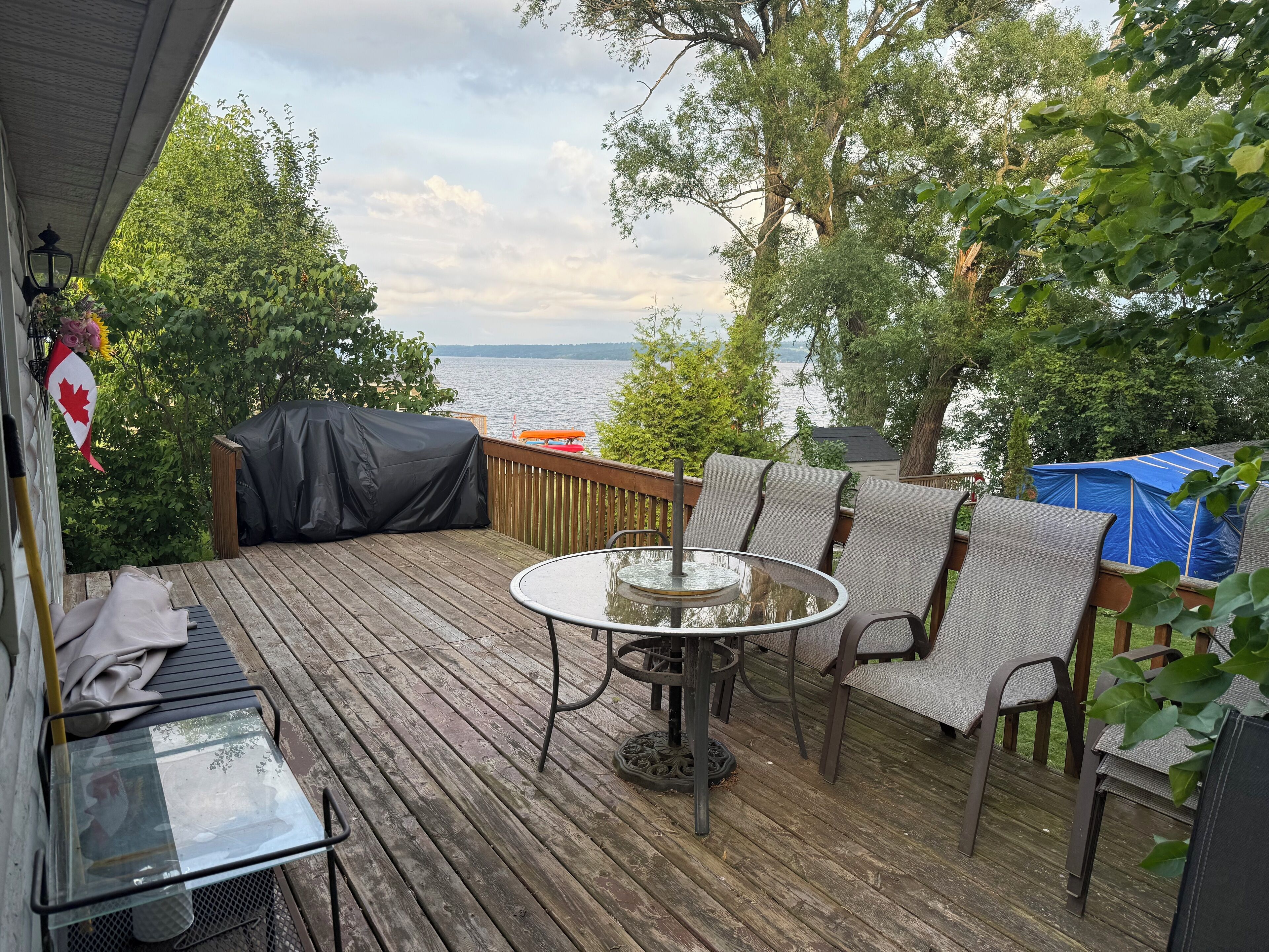 Una terraza de madera con una mesa y sillas de vidrio, con vistas a un lago.