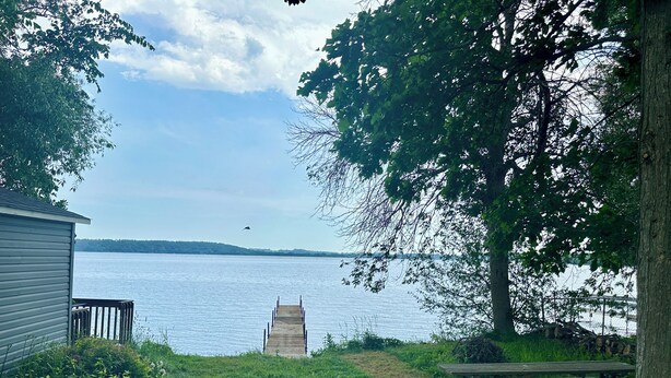 Une vue sur le lac, avec une jetée en bois qui s’avance dans l’eau, une table de pique-nique et un petit bâtiment.