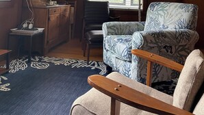 A living room with a wooden cabinet, a black leather chair, a patterned armchair, a wooden coffee table, and a floor lamp. - Beach garden cottage with AC in charming Ogunquit (Ogunquit)
