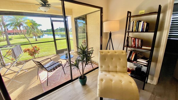 Un salon moderne doté d’une grande porte vitrée donnant sur une terrasse, d’un fauteuil capitonné, d’un lampadaire et d’une bibliothèque.