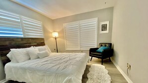 Une chambre avec un grand lit, une chaise dotée d’un coussin bleu et une lampe fixée au mur.