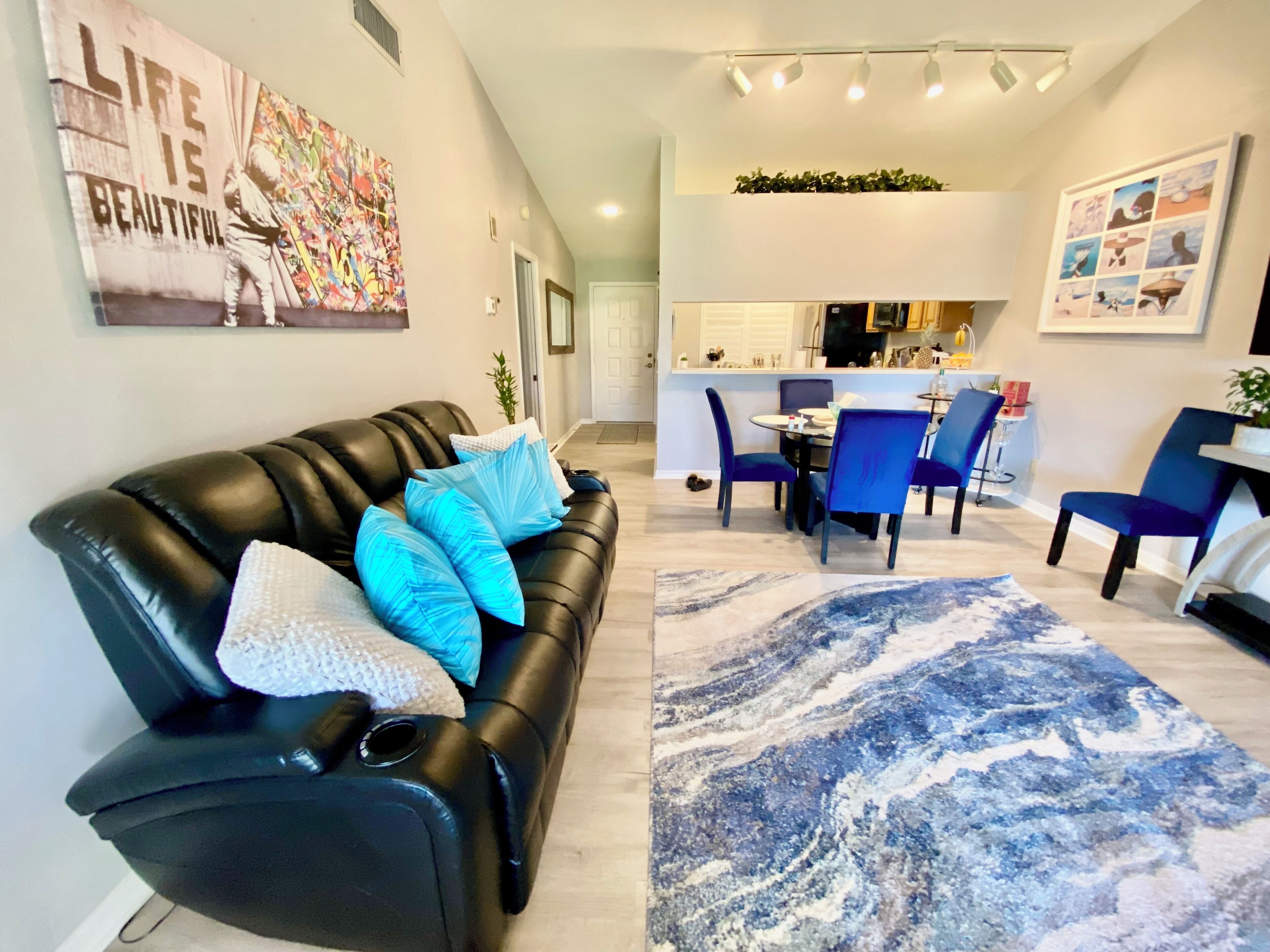 A modern living room with a black leather sofa, blue cushions, a marble-patterned rug, and a dining area with blue chairs.
