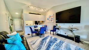 Un salon moderne avec un canapé en cuir noir, un tapis à motifs bleus et un coin repas avec des chaises bleues.