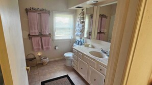 A bathroom with a toilet, sink, and vanity. There are towels hanging on a rack and a mirror above the sink.