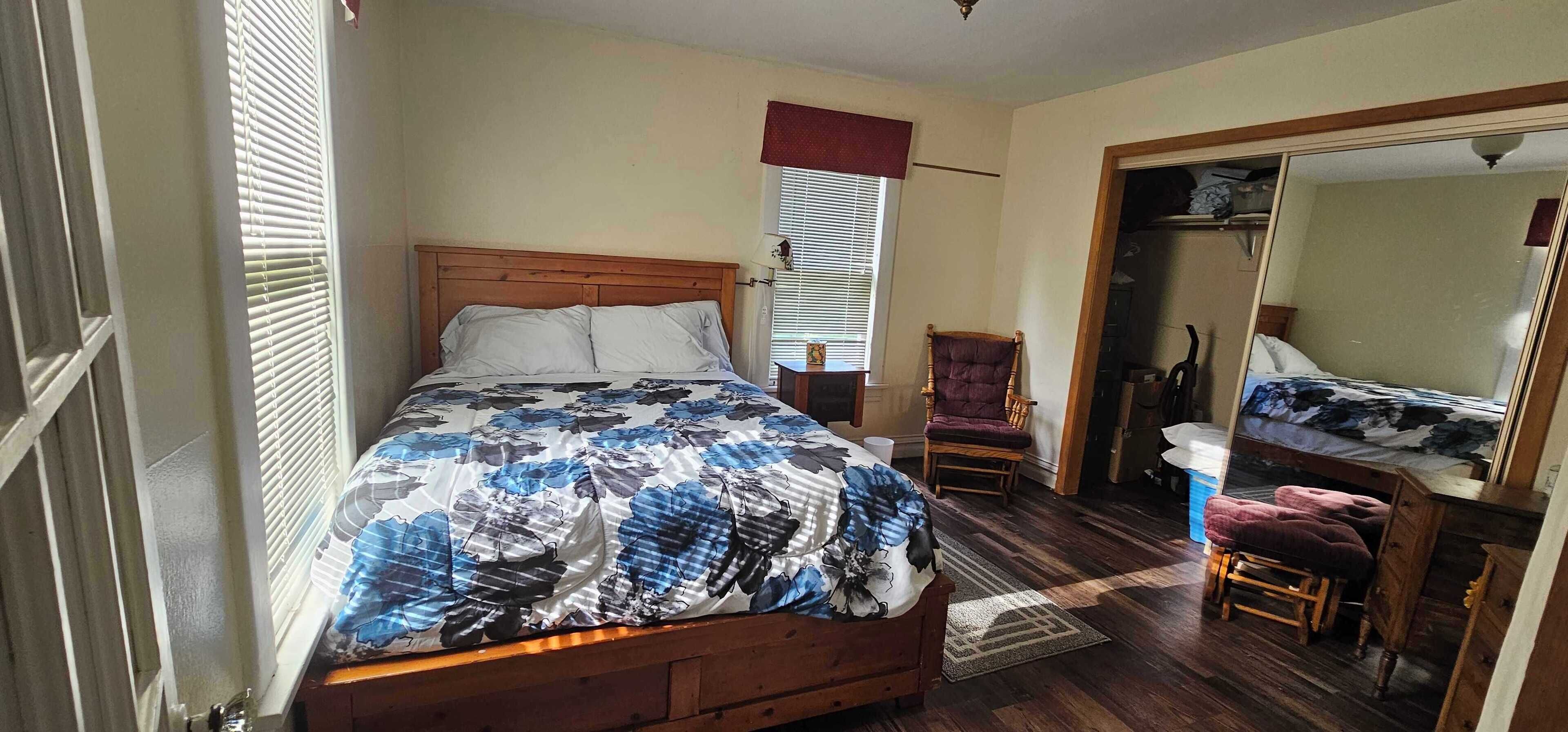 Une chambre à coucher avec un lit en bois, une chaise, un bureau et un miroir.