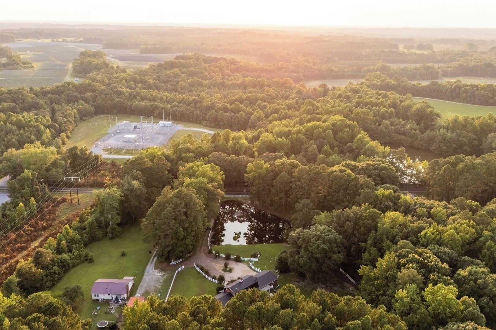 An aerial view of a rural property with a large field, a small pond, and a fenced area with a building.
